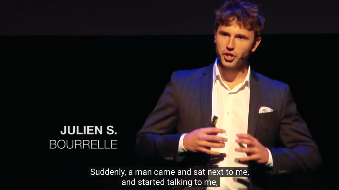 Julien S Bourrelle in a screenshot from his TEDx Talk Culture Drives Behaviours. He's in a dark suit with his hands in front of him as he speaks.